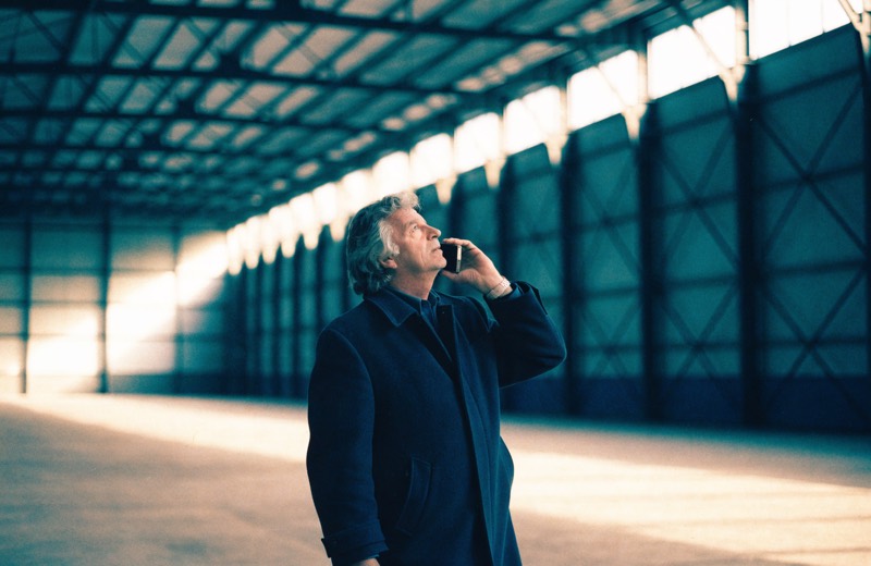 Een taxateur staat in een lege bedrijfshal en spreekt in zijn telefoon, kijkend naar de stalen spanten.