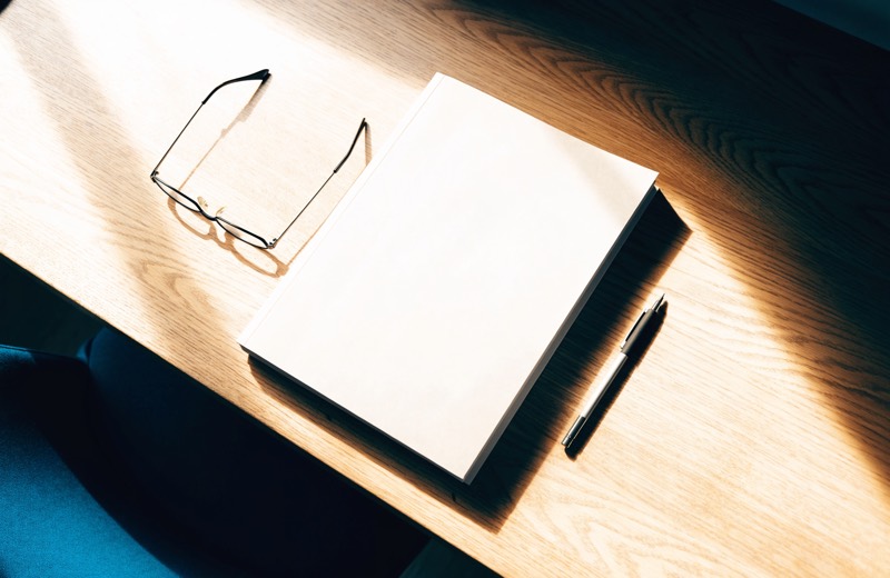 Een gedrukt taxatierapport ligt dichtgeslagen op een eiken bureau, met een leesbril en een vulpotlood ernaast.